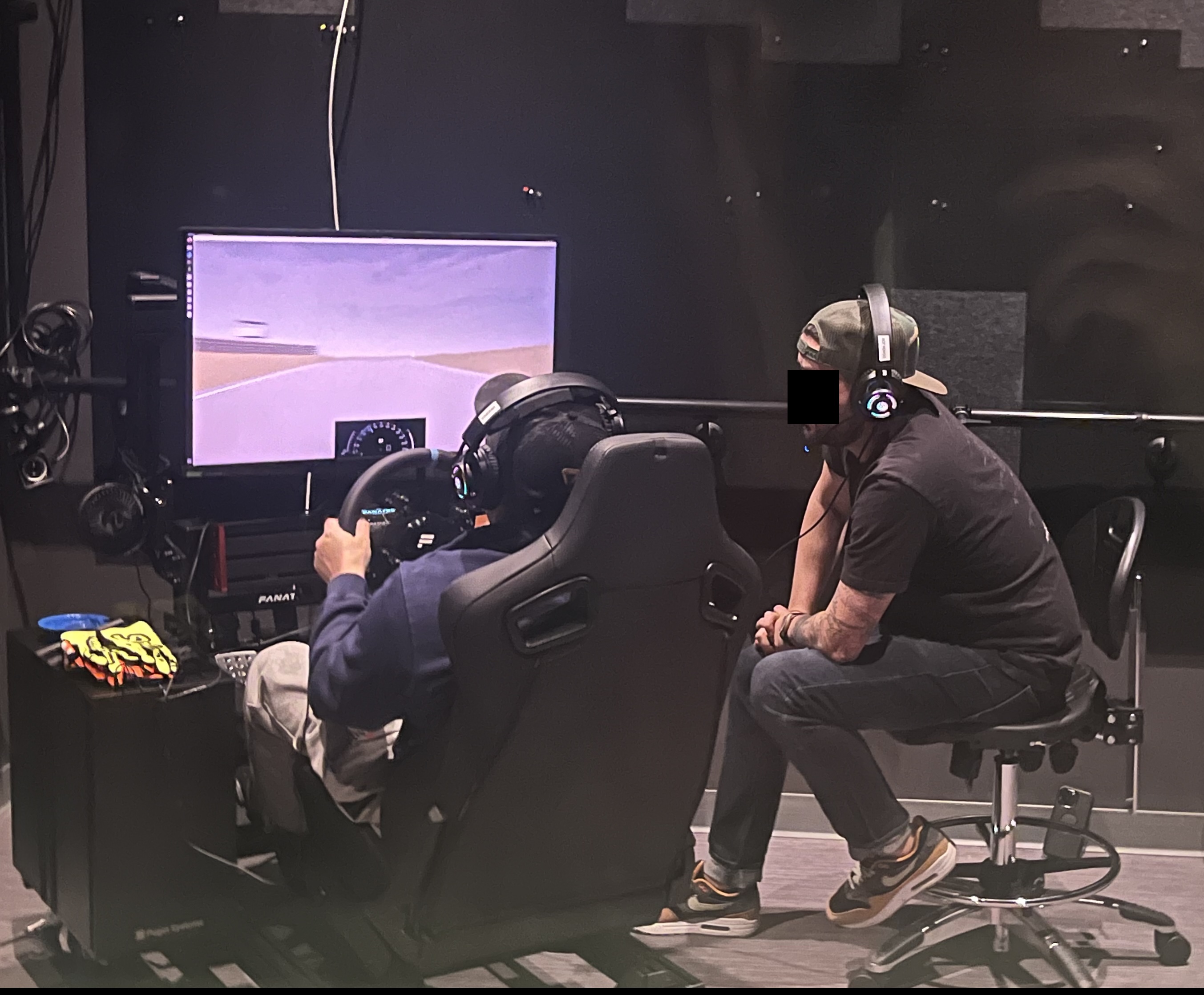 A professional driving coach observes and instructs a participant driving in the racing simulator.